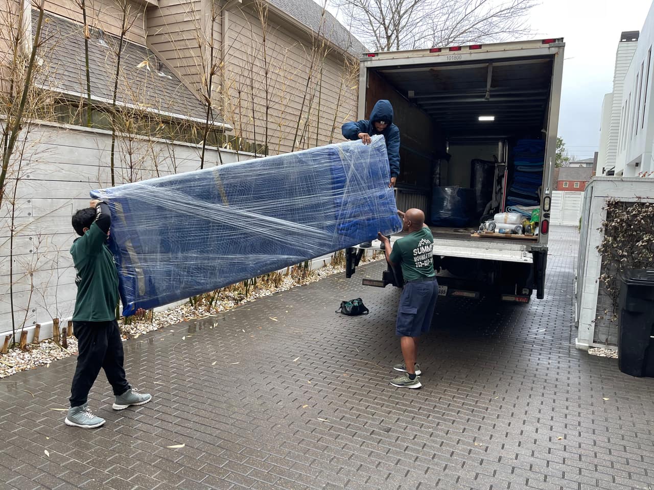 Three Summit crew members carrying a blanket-wrapped table down the ramp of a moving truck
